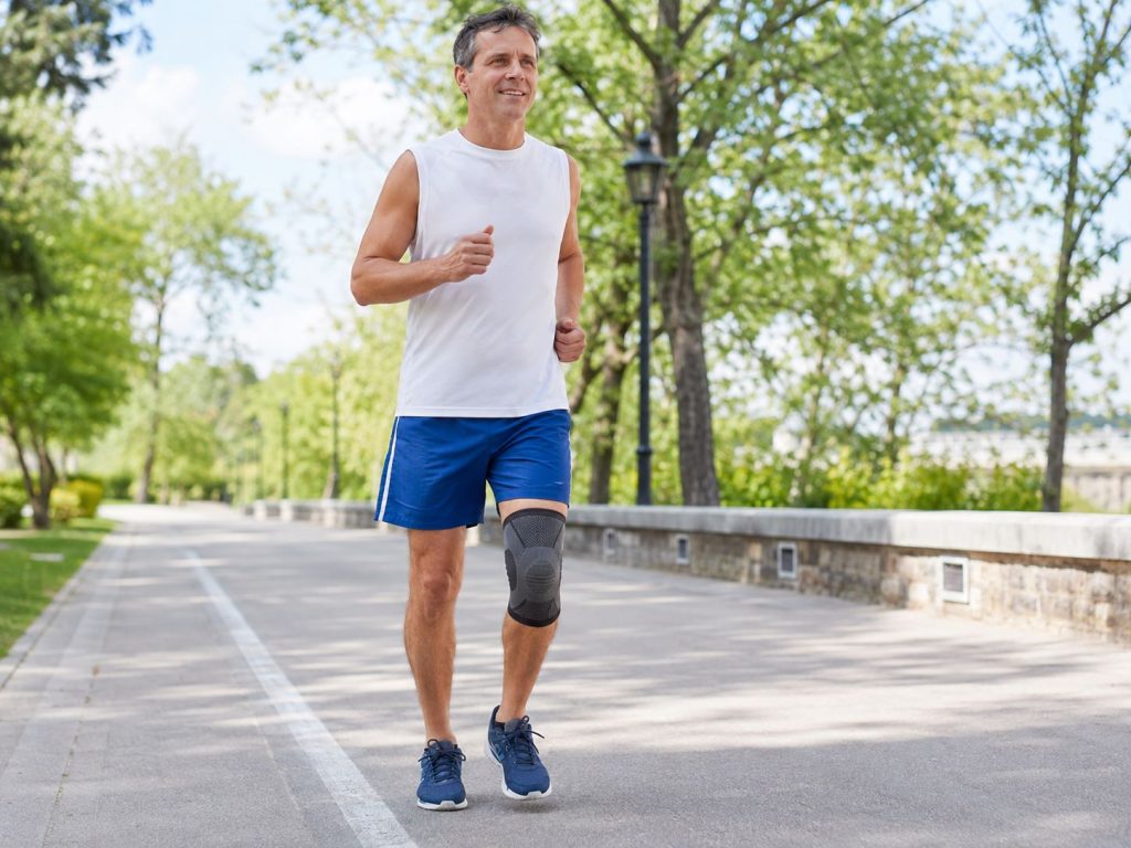 Hombre trotando con rodillera en un parque. ejemplo de vuelta segura al deporte con soporte de rodilla